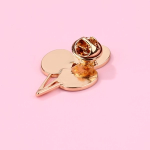 Close-up of rose gold cherry brooch with secure butterfly clasp on pink backdrop