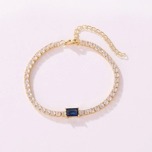 Detailed view of a gold tennis bracelet with clear zircons and a central rectangular blue stone.