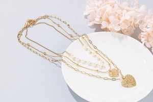 Detail of layered gold heart necklaces and pearl chains on a white ceramic plate