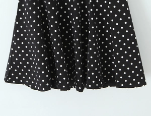 Détail du tissu noir léger avec motif à pois blancs et ourlet à volants sur la robe