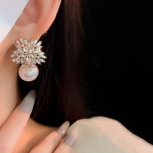 Close-up of golden snowflake earrings with rectangular diamonds and large white pearl