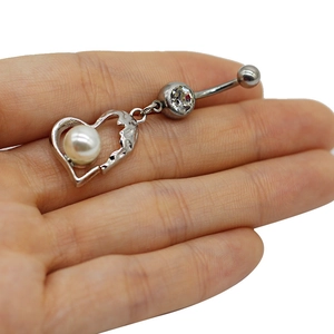 Macro detail of silver heart belly ring with white pearl and sparkling zircon stone