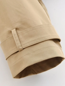 Close-up of khaki trench coat sleeve with detailed stitching and twill fabric texture