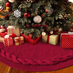 Detailed close-up of dark red chunky knit Christmas tree skirt on warm wooden floor