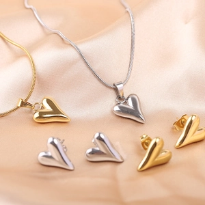 Detail of polished gold and silver heart necklaces and stud earrings on beige silk fabric