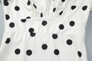Dettaglio dello scollo a V e del corpetto arricciato sull'abito bianco a pois con maniche a campana