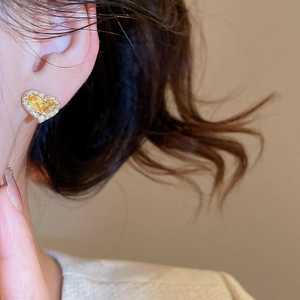 Detailed view of heart-shaped gold earring with yellow gemstone and white pavé crystals