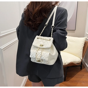 White quilted mini backpack with golden chain straps shown on a model in a black blazer