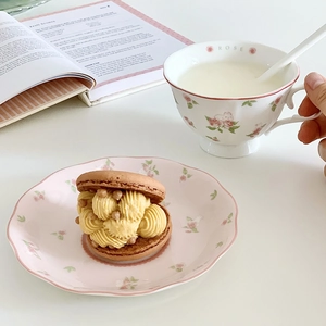 Detail of pink rose pattern ceramic coffee cup and saucer set with a macaron on a white table