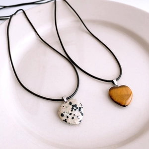 Détail de pendentifs en forme de cœur en œil de tigre et jaspe dalmatien sur cordons noirs