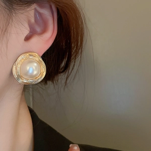 Detailed close-up of large round pearl earring with vintage gold spiral textured metal base