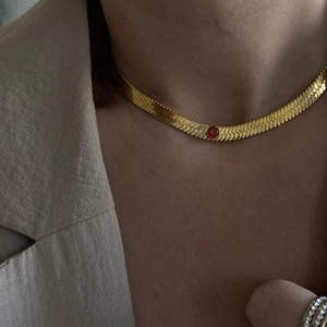 Close-up of a gold flat snake chain necklace with a round red gemstone pendant on a woman