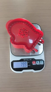 Kitchen tool weight detail of a red 3D Christmas tree cookie mold on a scale