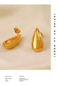 Macro shot of polished 18K gold stainless steel teardrop earrings on textured fabric
