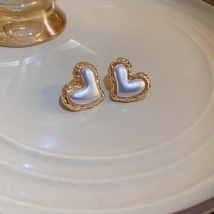 Close-up of heart-shaped gold earrings with pearlescent center on a ceramic tray