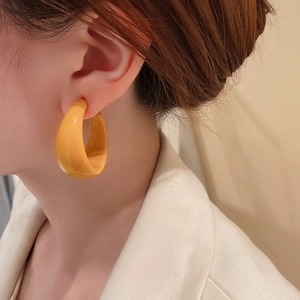 Close-up of a model wearing a thick yellow hoop earring with a smooth glossy finish