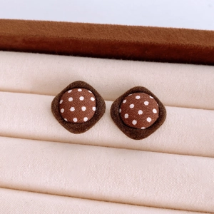 Macro shot of brown fabric button stud earrings with white polka dots on beige velvet