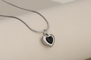 Macro shot of silver snake chain necklace featuring a heart pendant with black crystal