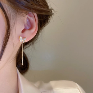 Close-up of elegant gold butterfly tassel earrings worn by a model in warm lighting