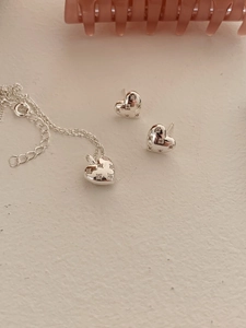 Detail view of a silver heart jewelry set featuring a zircon-inlaid necklace and stud earrings