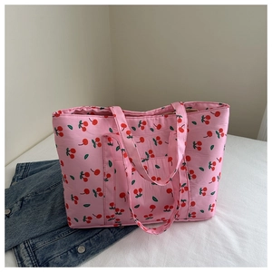 Detailed view of pink tote bag with red cherry pattern on a casual denim jacket background