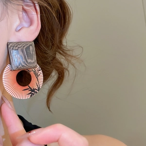 Detail of square wood and patterned resin hoop earrings worn on a female model