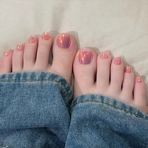 Close-up of Aurora pink press-on toenails on feet with blue jeans and beige bedding