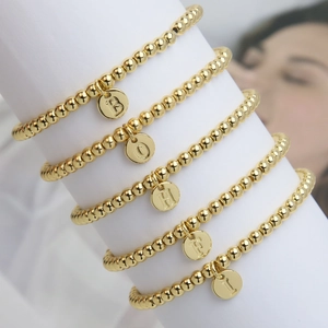 Polished gold beaded bracelets set with round alphabet charms on minimalist display