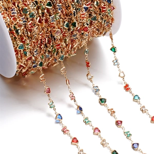 Macro detail of colorful crystal butterfly and heart charms on a golden DIY jewelry chain