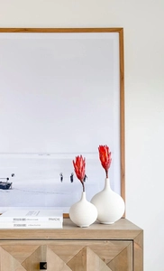 Moderne weiße Keramikvasen mit Rillenstruktur und roten Protea-Blumen auf einem Holzschreibtisch