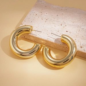 Close-up of gold layered C-shaped hoop earrings on beige textured stone display