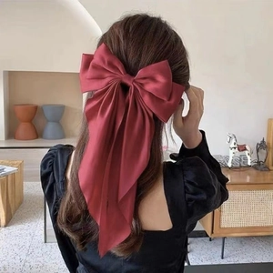 Detailed view of a large red satin bow hair clip with long ribbons on model's hair