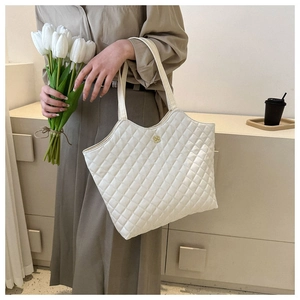 Détail d'un grand cabas matelassé blanc avec logo fleur en métal sur fond beige doux
