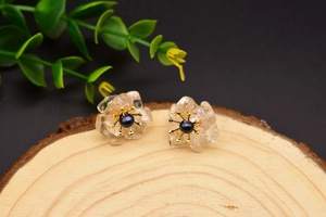Macro shot of pearl flower earring with pink petals and gold details on wood stand