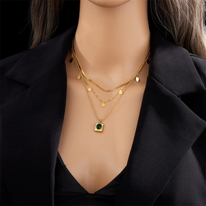 Detail of emerald green pendant and layered gold snake chains on a model with soft lighting