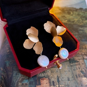 Macro detail of golden flower earrings with baroque pearls on red velvet display