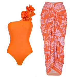 Close-up of orange one-shoulder swimsuit with 3D floral accent and tropical wrap skirt