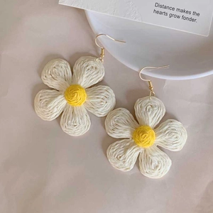 Detailed view of handmade daisy drop earrings with white petals and woven texture