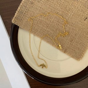 Close-up of a gold bird pendant necklace on a ceramic dish with adjustable clasp detail
