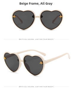 Detail of beige heart-shaped sunglasses featuring golden bee accents and grey lenses
