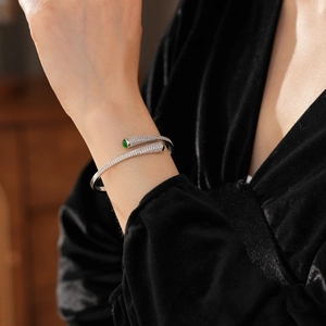 Detail of silver open bangle with pavé zircons and a round green emerald stone