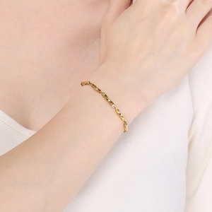 Detail of a gold-plated twisted Chopin chain bracelet on a model's wrist with a metal finish
