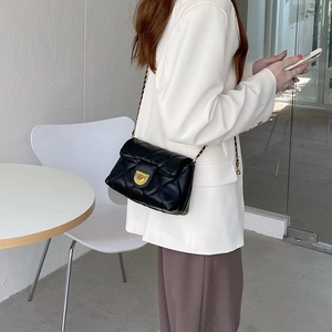 Detail shot of black quilted shoulder bag with gold chain strap on a white blazer