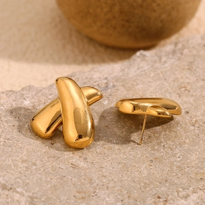 Macro shot of minimalist gold-plated stainless steel X-shaped earrings on textured stone
