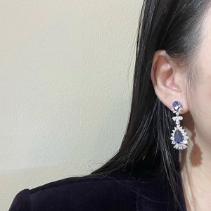 Macro view of teardrop blue gemstone earrings with silver diamond setting on female model