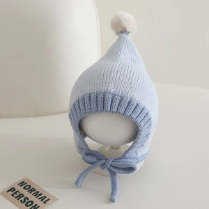 Close-up of color-block knit baby hat with pointed top, pompom, and chin straps