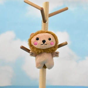 Cute plush lion keychain hanging on a decorative wooden stand against a blue sky background