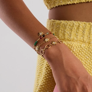 Close-up of a stack of four gold bracelets with sun pendant and rhinestones on a wrist