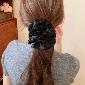 Détail d'un chouchou noir en satin à volants porté sur une queue de cheval pour la coiffure