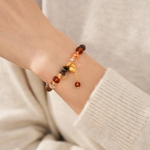 Détail du bracelet en perles d'œil de tigre avec breloque cloche dorée au poignet